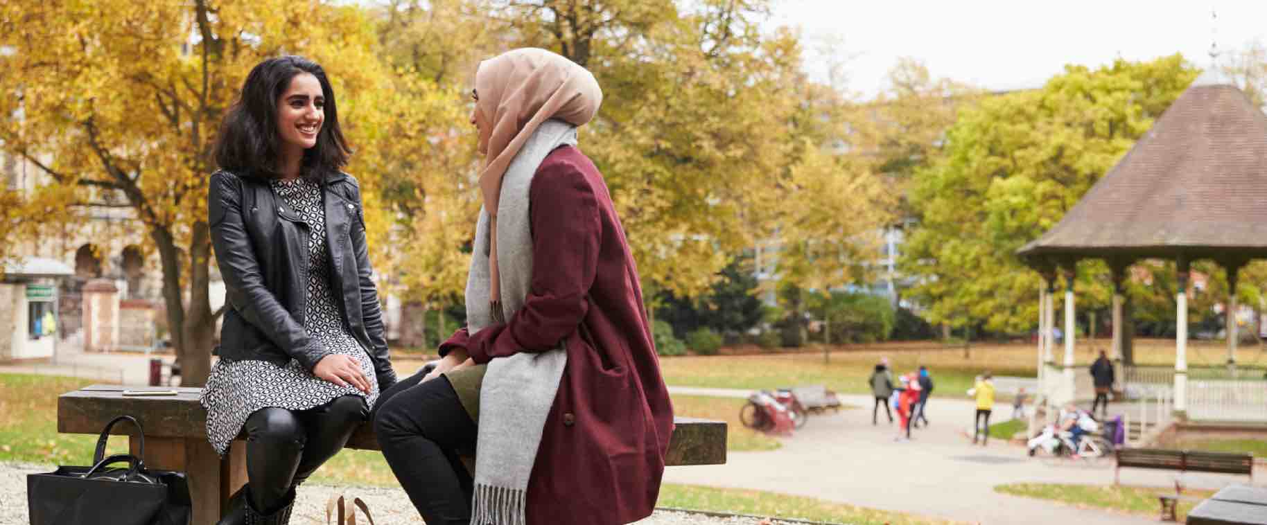 Two young women talking together on a bench in an urban park