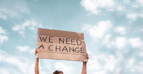 Women holding a board with 'we need a change' on it