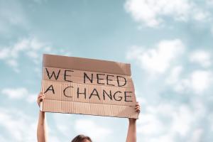 Women holding a board with 'we need a change' on it